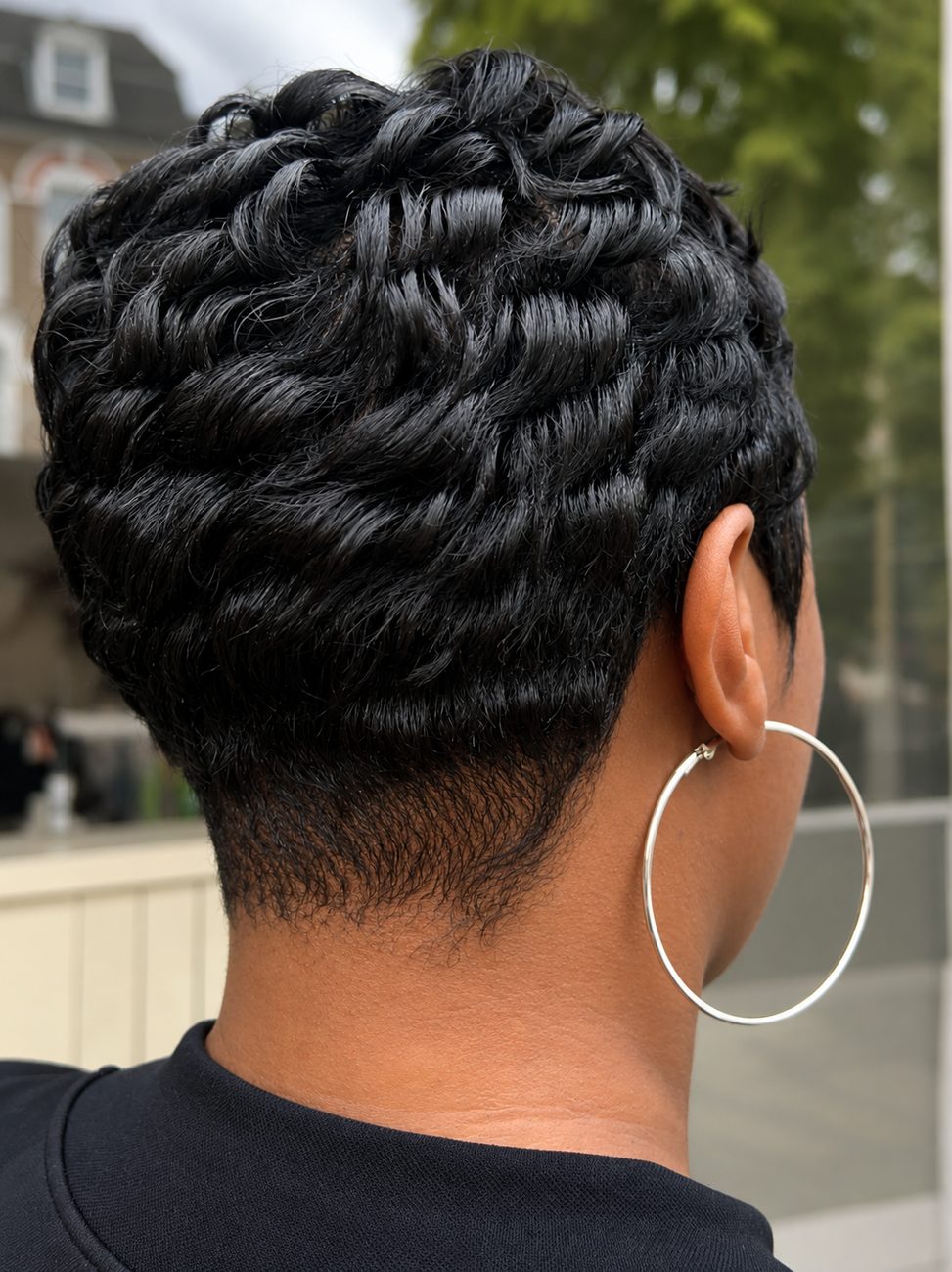 Back view of a softly curled short pixie with a sharp nape and a silver hoop earring